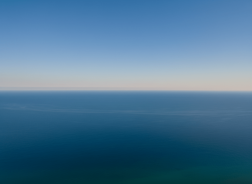 A vast infinite deep blue ocean horizon, calm water, clear sky, photorealistic, wide landscape, no people, serene and majestic